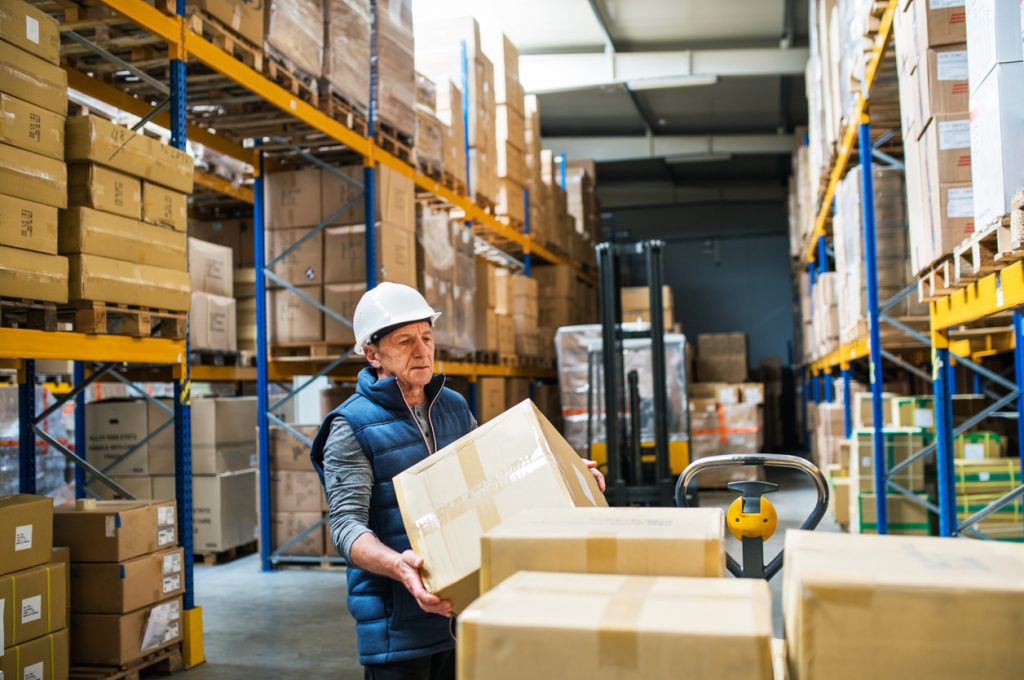 Senior male warehouse worker unloading boxes from a pallet truck.